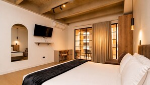 Une chambre d’hôtel dotée d’un grand lit, d’un téléviseur à écran plat fixé au mur, d’un bureau avec une chaise et d’une fenêtre avec des rideaux.