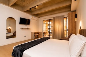 Ein Hotelzimmer mit einem großen Bett, einem wandmontierten Flachbildfernseher, einem Schreibtisch mit Stuhl und einem Vorhangfenster.