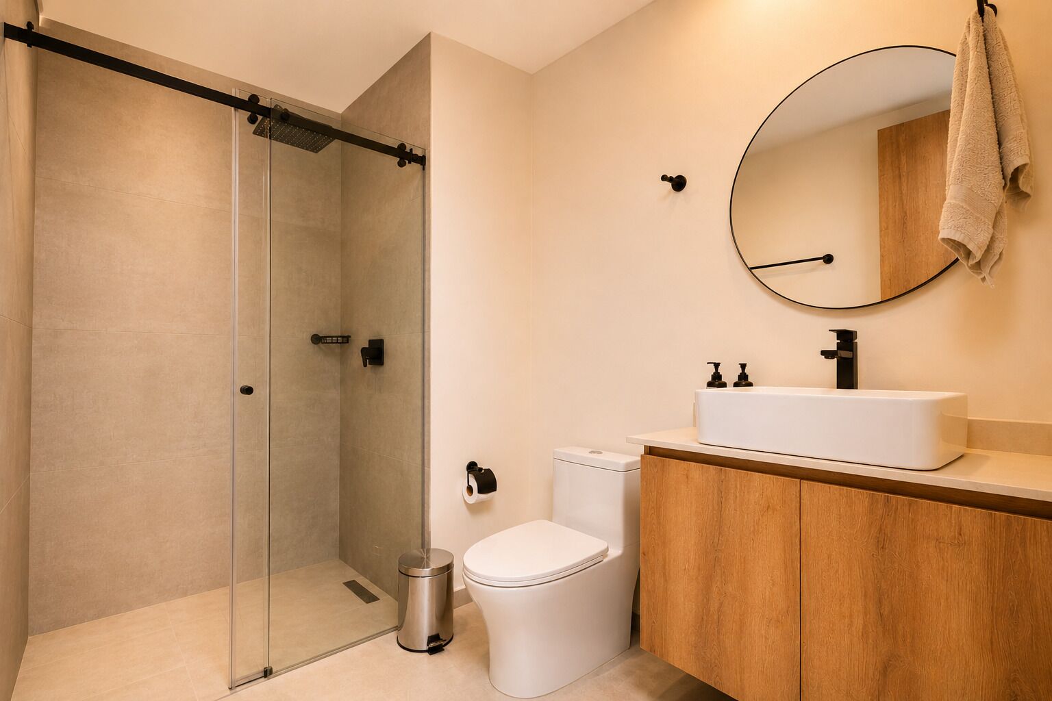 Un baño moderno con ducha envuelta en vidrio, inodoro blanco y tocador de madera con lavamanos.