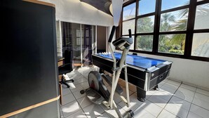 Habitación con mesa de fútbol, equipo de ejercicios y grandes ventanales con vistas a zonas verdes.