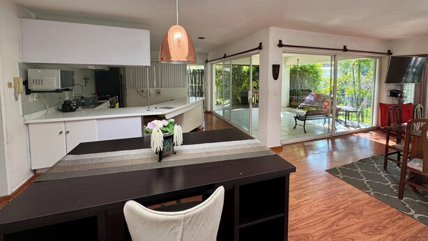 Una cocina moderna con encimera blanca, una lámpara colgante de cobre y vistas a un patio con mesa y sillas.