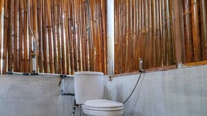 A bathroom with a toilet, bamboo wall, and concrete floor.