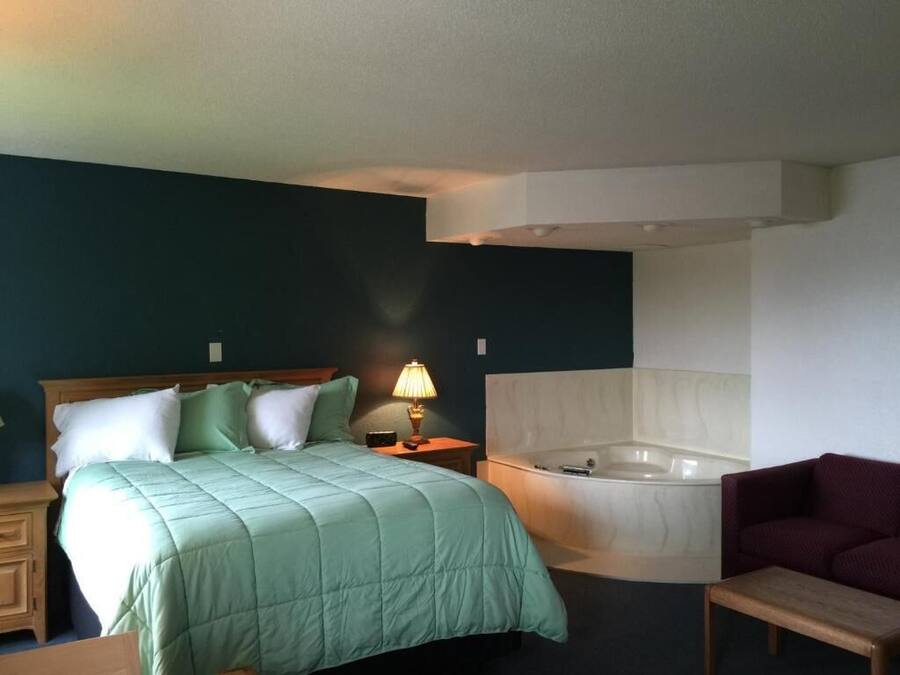 A hotel room with a bed, a nightstand, a lamp, a sofa, and a bathtub.