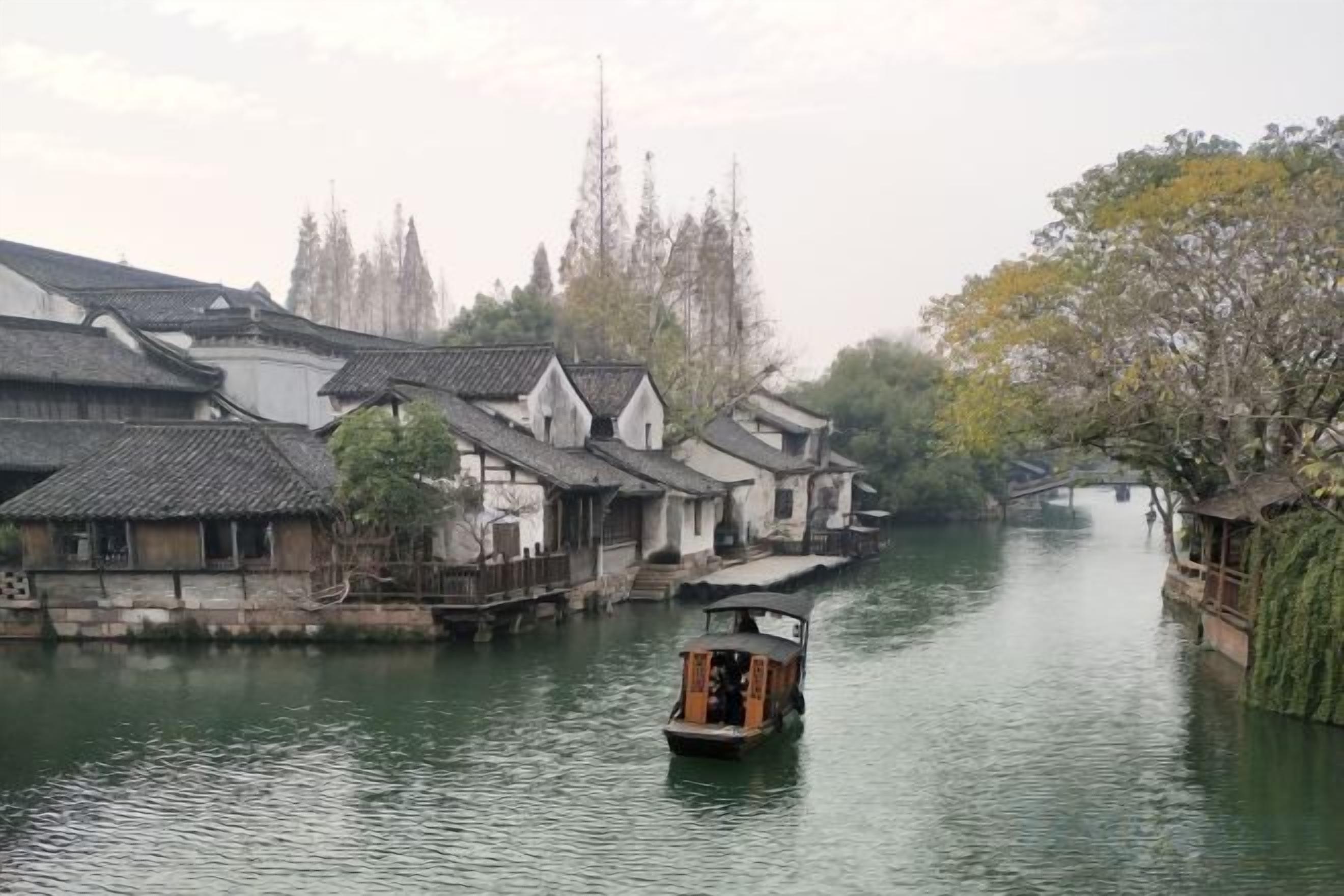 A traditional wooden boat on a calm river, surrounded by old-style buildings with tiled roofs.