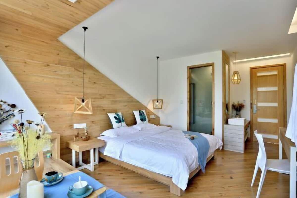 Ein Schlafzimmer mit schrägen Wänden, einem Bett mit weißer Bettwäsche, einem Schreibtisch mit Stuhl und einem kleinen Tisch mit einer Vase.