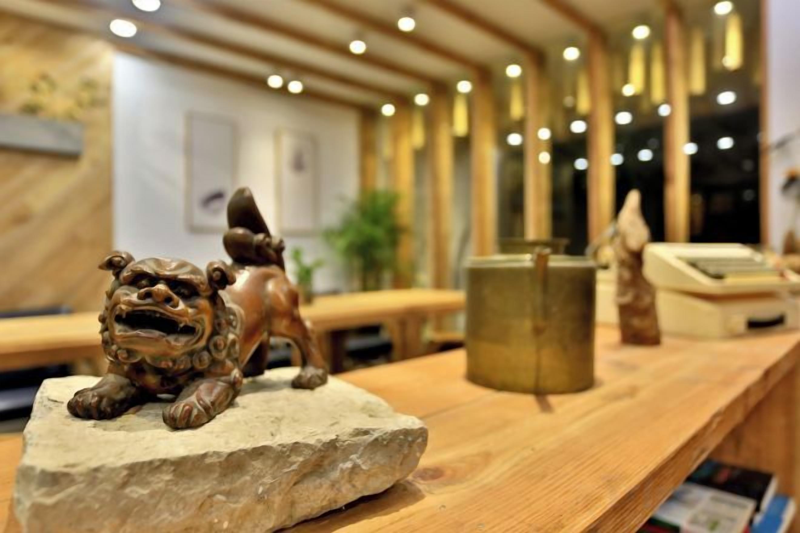 A wooden reception desk with a stone sculpture of a lion, a cash register, and a plant in the background.