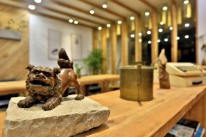 Un comptoir d’accueil en bois, agrémenté d’une sculpture en pierre représentant un lion, d’une caisse enregistreuse et d’une plante en arrière-plan.