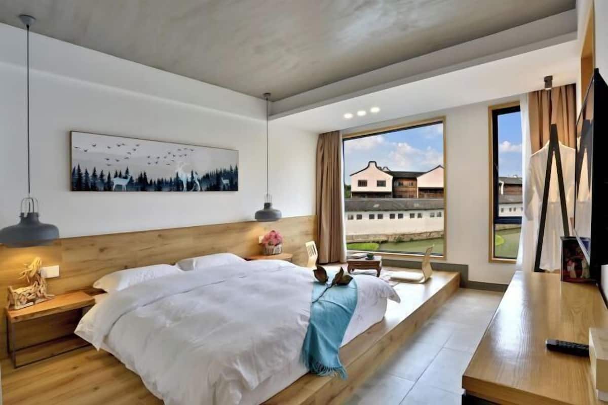 Ein modernes Hotelzimmer mit einem großen Bett, einem Schreibtisch, einem Fernseher und Blick ins Freie.