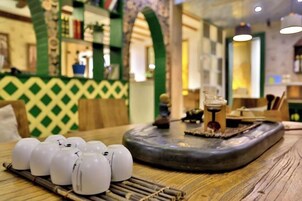 Una mesa con tazas de cerámica blanca y una bandeja decorativa, en una habitación con paredes de diseño verde y muebles de madera.