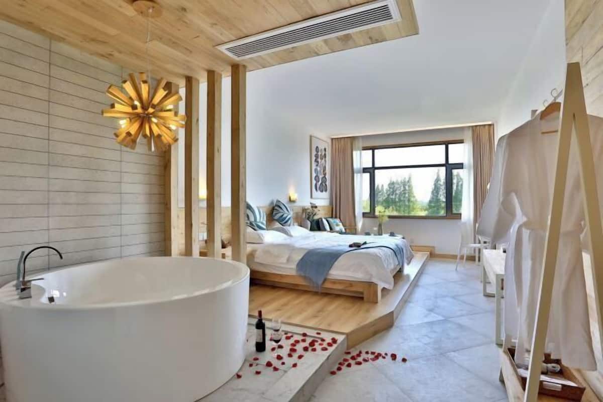 Ein modernes Schlafzimmer mit einer großen Badewanne, einem Bett mit Blick ins Freie und einer Holzbalkendecke.