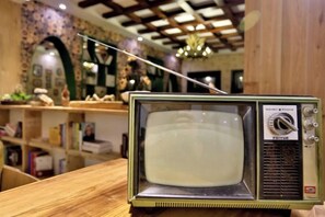 En gammal TV-apparat står på en träyta, med en hylla och dekorativa föremål i bakgrunden.