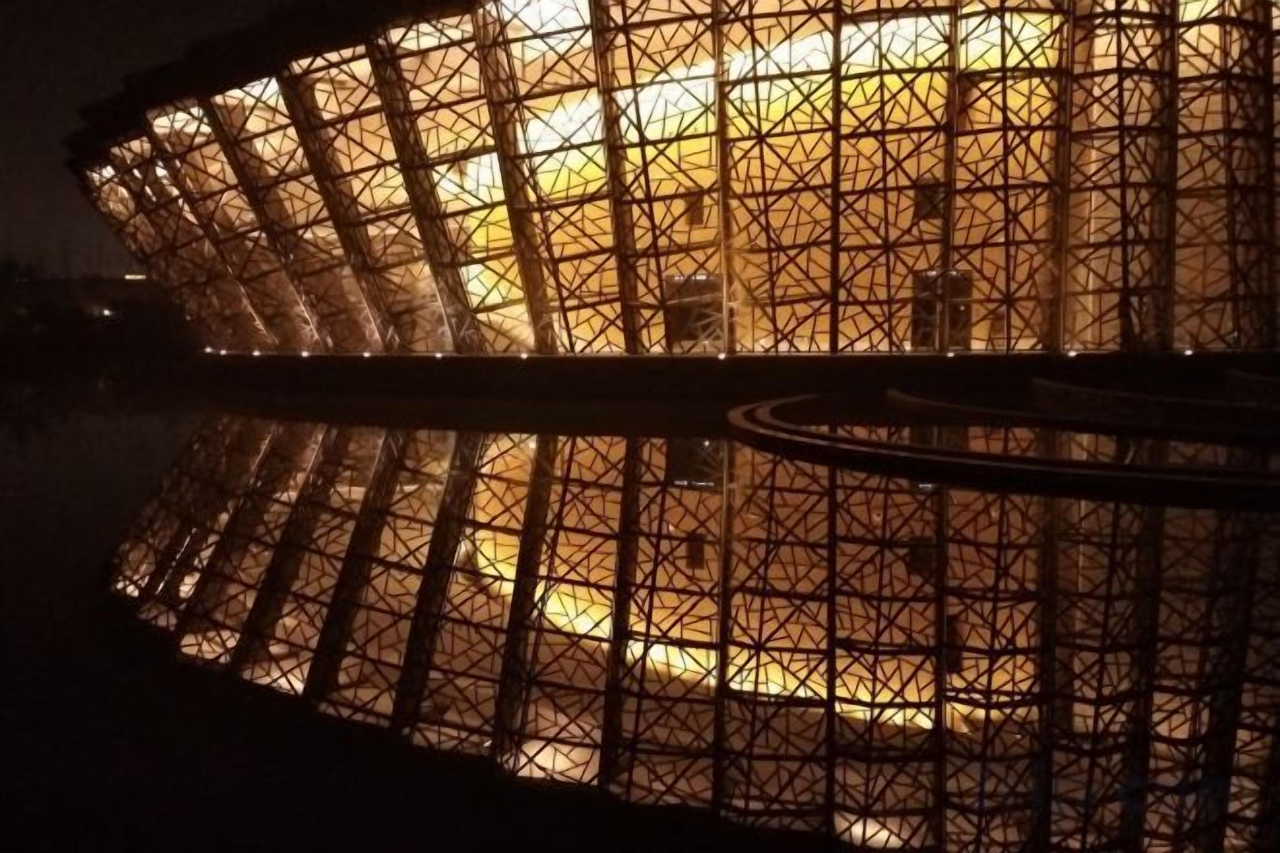 A large, circular structure with a grid-like pattern, reflecting on a body of water.