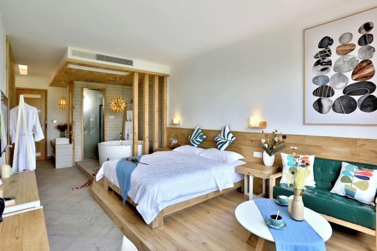 Une chambre d’hôtel moderne avec un lit en bois, un canapé vert, une petite table et une œuvre d’art murale.