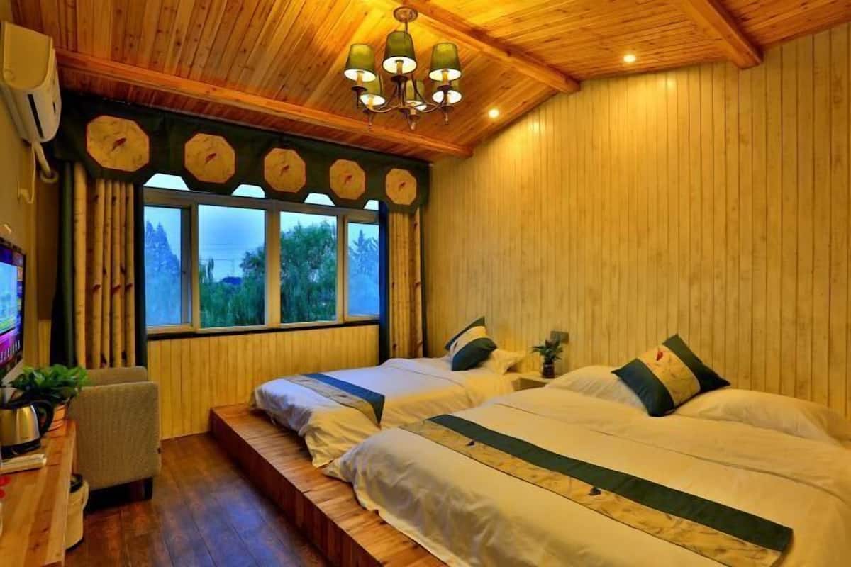 Ein Zimmer mit Holzwänden und -decke, zwei Betten mit weißer und grüner Bettwäsche, ein Holztisch mit Stuhl, ein Fernseher und ein Fenster mit Vorhängen.