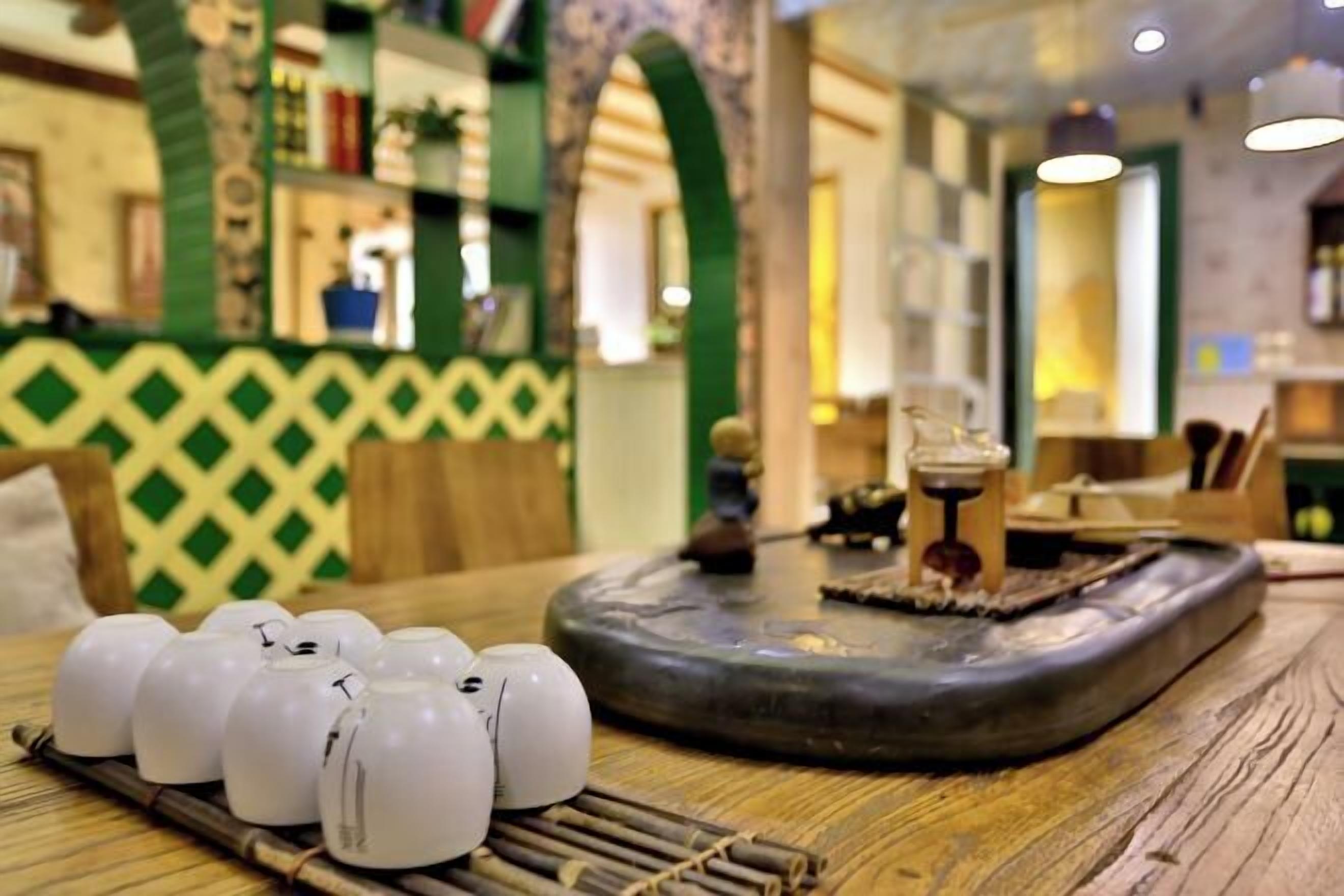 Un juego de té tradicional con teteras y una tetera sobre una mesa de madera, situado en una habitación con paredes de diseño verde y un arco decorativo.