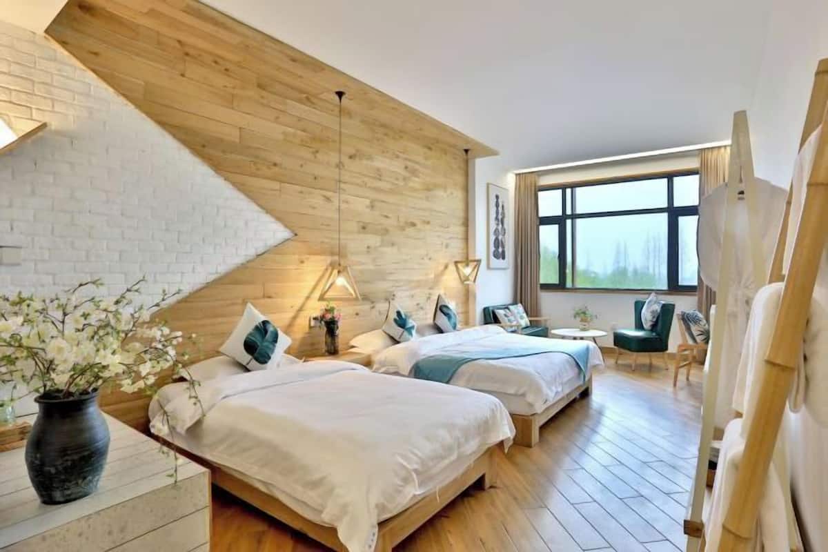 Ein Hotelzimmer mit zwei Betten, Holzboden, einem großen Fenster und einer Wand mit Ziegeln.