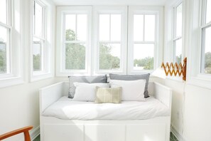 A bright room with a white bed, multiple windows, and a wooden chair. - Modern home with lookout in the heart of downtown (Wilmington)