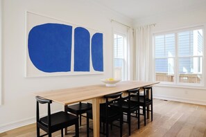 A dining area with a long wooden table, black chairs, and a large abstract painting on the wall. - Modern home with lookout in the heart of downtown (Wilmington)