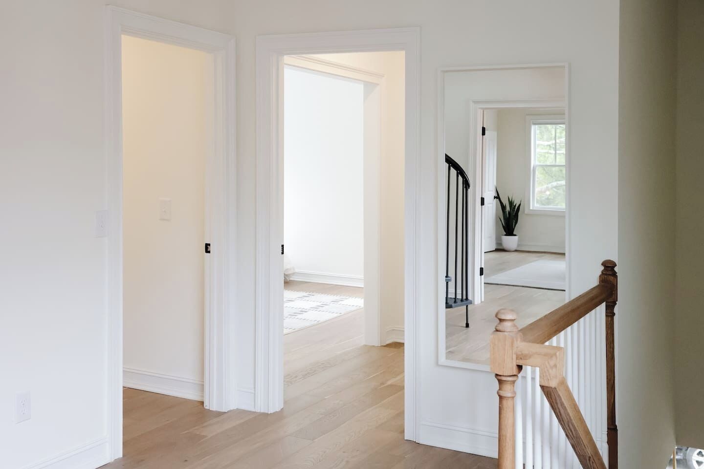 A hallway with wooden flooring, white walls, and a staircase with a wooden railing.