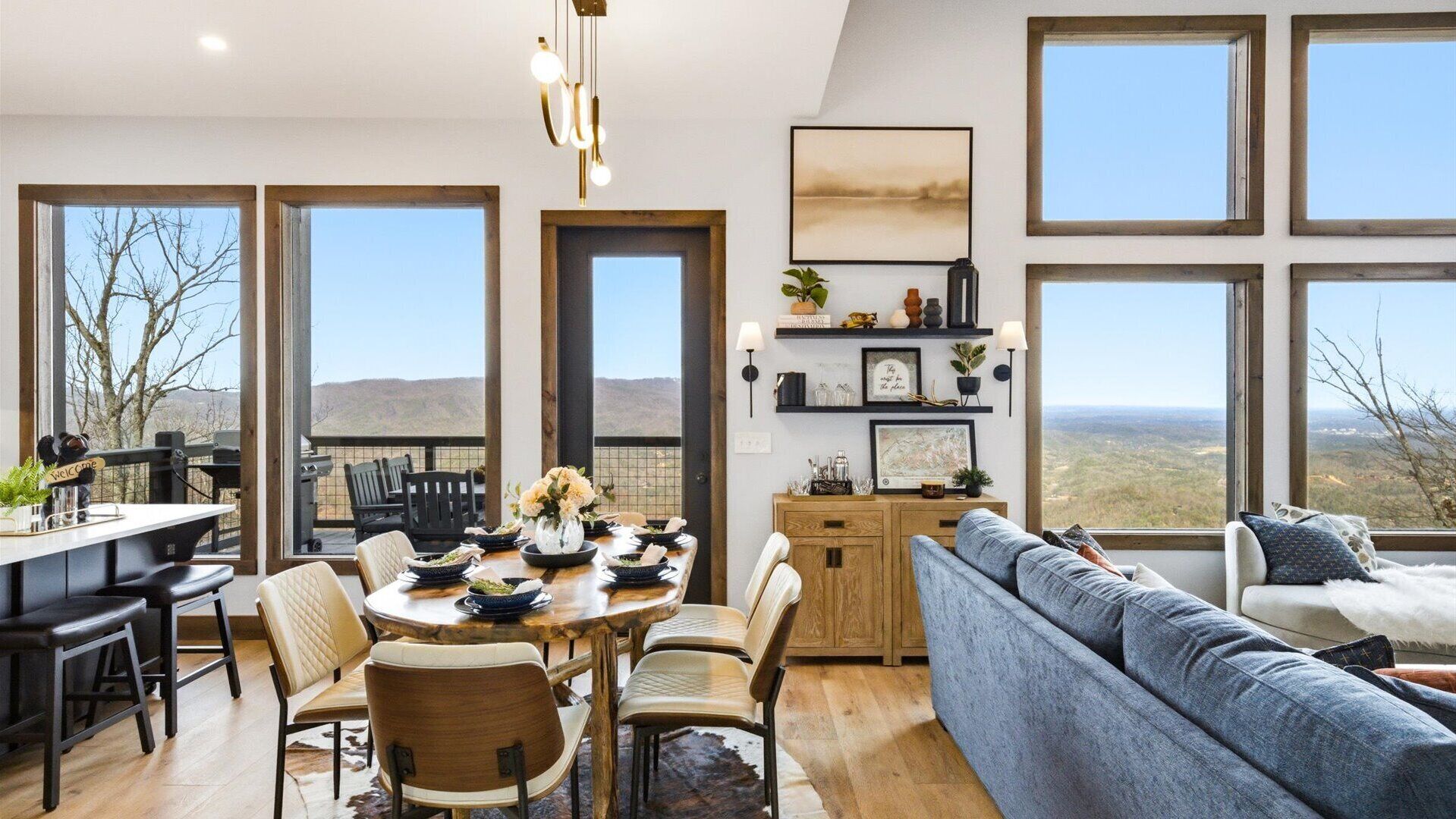 A spacious dining area with a wooden table and chairs, a sofa, and a view of the mountains.