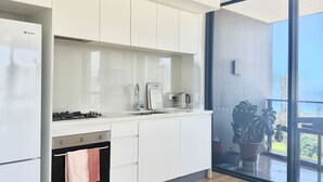 A modern kitchen with white cabinets, a gas stove, a sink, and a coffee maker. -  Coastal Luxe Apartment with Ocean & River Views (Surfers Paradise)