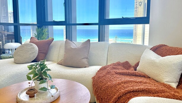 A modern living room with a large window overlooking a cityscape and the ocean. -  Coastal Luxe Apartment with Ocean & River Views (Surfers Paradise)