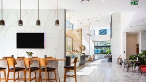 A spacious lobby with a reception desk, a seating area with wooden chairs, and a large TV screen. -  Coastal Luxe Apartment with Ocean & River Views (Surfers Paradise)