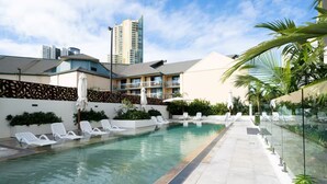 A swimming pool with lounge chairs, surrounded by a glass barrier and palm trees. -  Coastal Luxe Apartment with Ocean & River Views (Surfers Paradise)