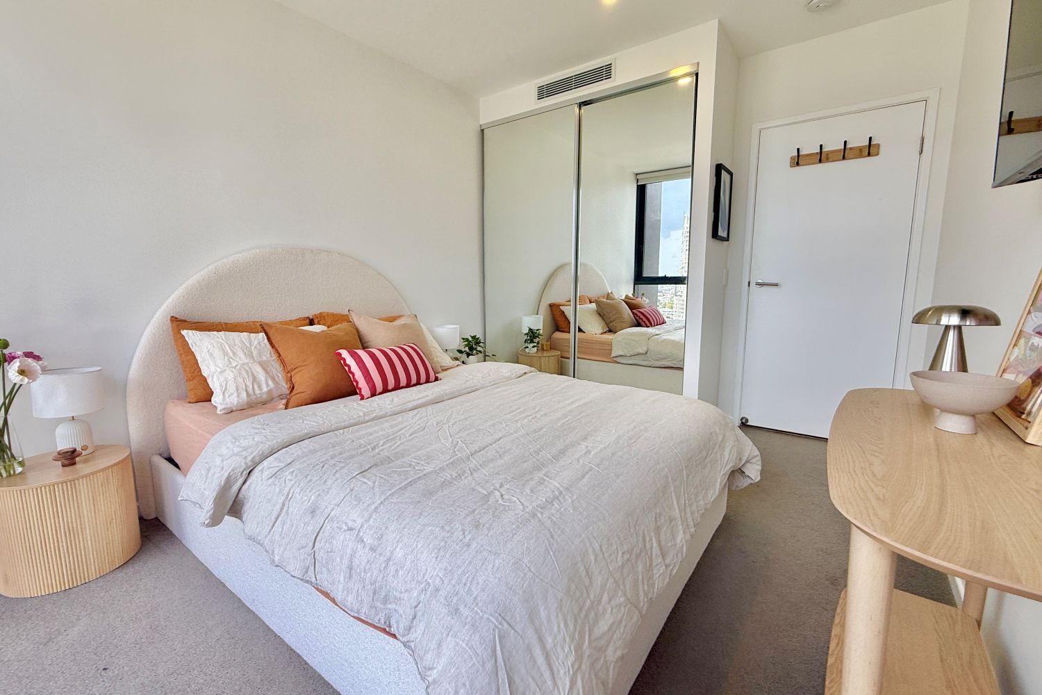 A modern bedroom with a large bed, a bedside table, a mirror, and a wardrobe.