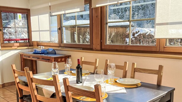 A dining area with a table set for four, wooden chairs, and a bottle of wine. - Blauer Elefant by Interhome (Kitzbühel)