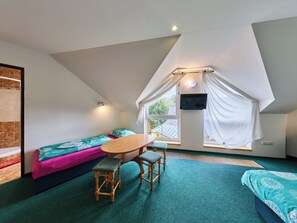Ein gemütliches Zimmer mit schrägen Wänden, einem Bett, einem Tisch mit Stühlen und einem an der Wand befestigten Fernseher.