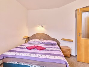 Ett sovrum med en säng, sängbord, en trädörr och en väggmonterad lampa.