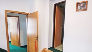 Habitació amb una cadira de fusta, una porta amb un llaveros vermell i un quadre amb marc a la paret.