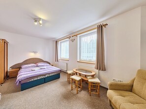 Ett sovrum med en säng, ett skrivbord med en stol, en soffa och stora fönster med gardiner.