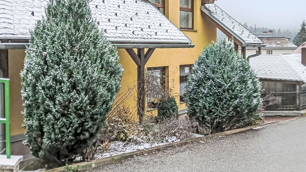 Una casa groga amb teulada inclinada i un porxo.