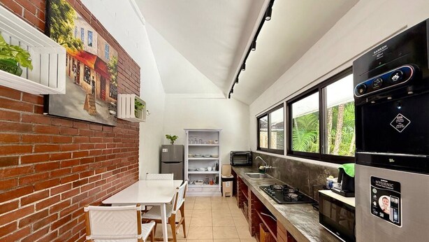 A kitchen with a brick wall, a dining area with a table and chairs, a refrigerator, a microwave, and a window with a view of greenery. - Villa White Orchid - Enclosed living area - Seminyak center - Quiet Private Pool (Seminyak)
