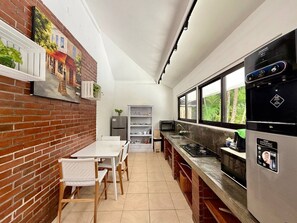 A kitchen with a brick wall, a dining area with a table and chairs, a refrigerator, a microwave, and a window with a view of greenery. - Villa White Orchid - Enclosed living area - Seminyak center - Quiet Private Pool (Seminyak)
