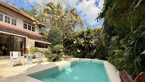 A swimming pool with a tiled deck, surrounded by lush greenery and a building with a tiled roof. - Villa White Orchid - Enclosed living area - Seminyak center - Quiet Private Pool (Seminyak)