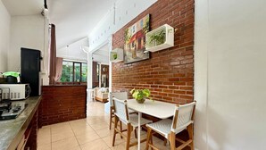 A kitchen with a brick wall, white cabinets, and a dining area with a table and chairs. - Villa White Orchid - Enclosed living area - Seminyak center - Quiet Private Pool (Seminyak)
