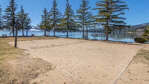 Una spiaggia sabbiosa con un campo da pallavolo e una rete, circondata da alberi alti e un lago sullo sfondo.