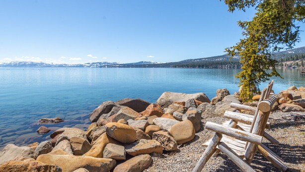 Vista su un lago con una panchina di legno e rocce in primo piano.