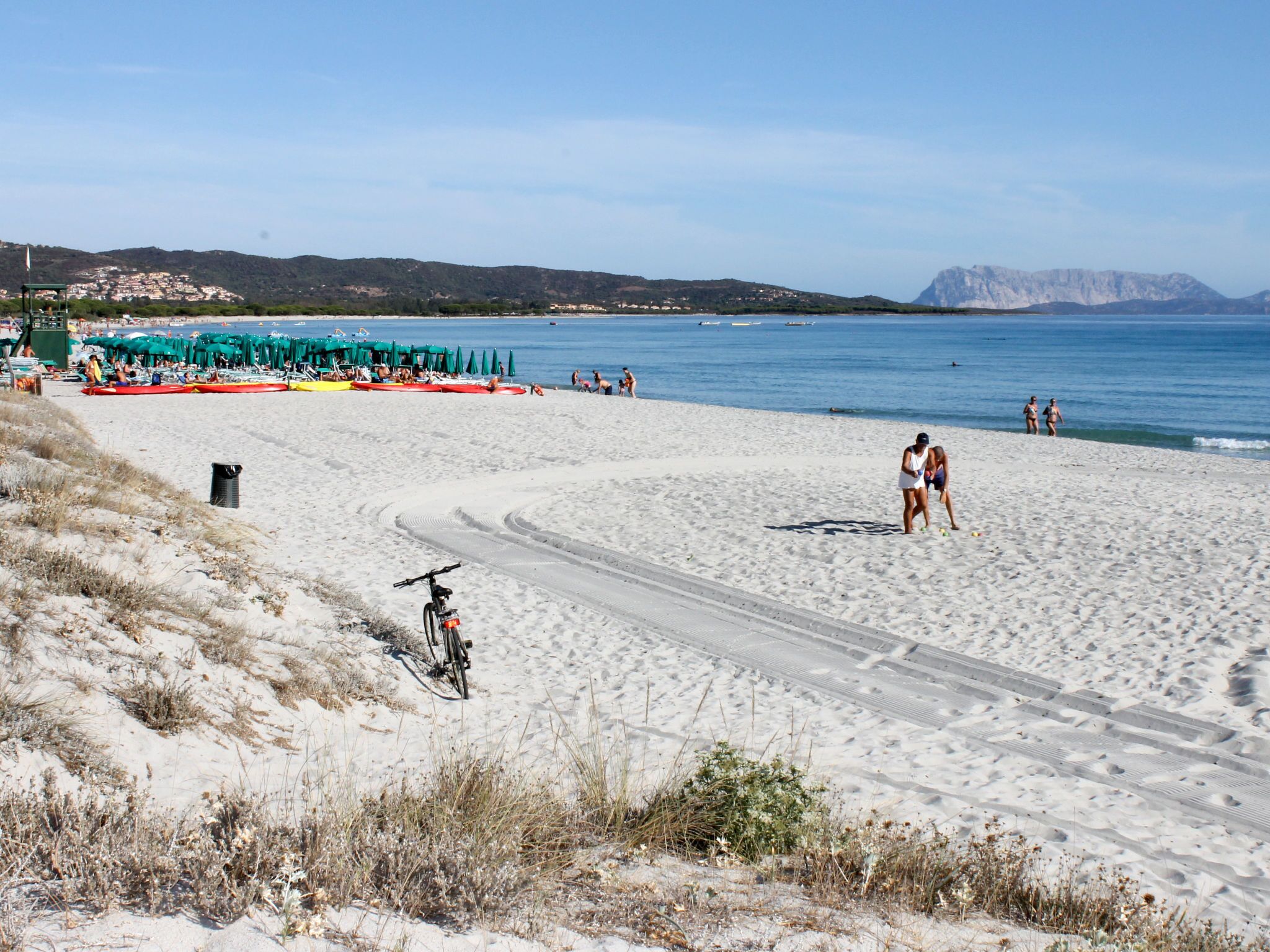 A beach with a bicycle path, beach umbrellas, and people walking.