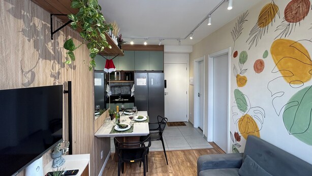 A modern living room with a flat-screen TV, a grey sofa, and a dining area with a table set for two. - Apartment in the heart of São Paulo (São Paulo)