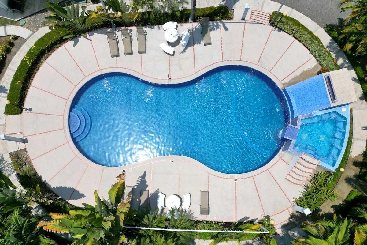 A large, circular swimming pool with a central island and surrounding lounge area, surrounded by palm trees and a paved deck.