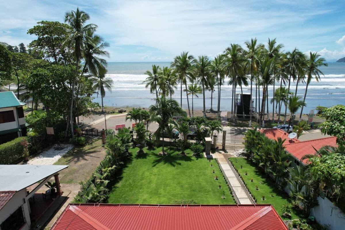 A view of a beachside property with a lawn, palm trees, and a building with a red roof.