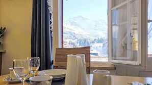 A dining table set with plates, cups, and a pitcher, overlooking a snowy mountain landscape through a window. - Chalet Graf Apt 1 by Interhome (Wengen)