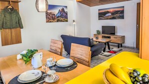 A modern living room with a dining area, featuring a wooden ceiling, a TV, and artwork on the walls. - Chalet Graf Apt 1 by Interhome (Wengen)