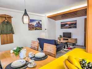 Ein modernes Wohnzimmer mit Essbereich, ausgestattet mit Holzboden, einem Fernseher und Kunstwerken an den Wänden.
