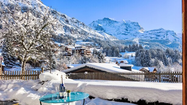 A snow-covered outdoor dining area with a table and chairs, surrounded by a wooden fence and snow-laden trees. - Chalet Graf Apt 1 by Interhome (Wengen)