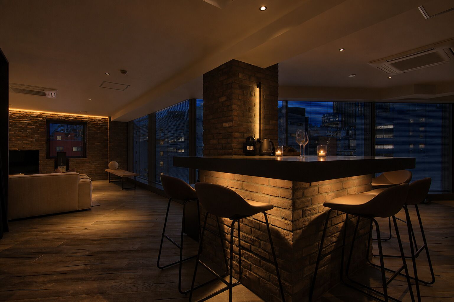 A modern bar area with a stone accent wall, bar stools, and a view of the city at night.
